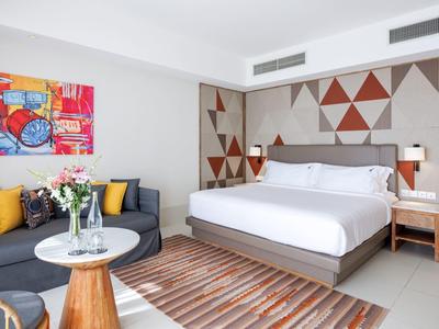 Modernes Schlafzimmer mit Doppelbett, geometrischer Wanddeko, grauem Sofa und buntem Bild an der Wand.