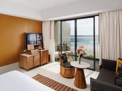 Modernes Wohnzimmer mit braunen Holzmöbeln, grauem Sofa und Balkon mit Meerblick.