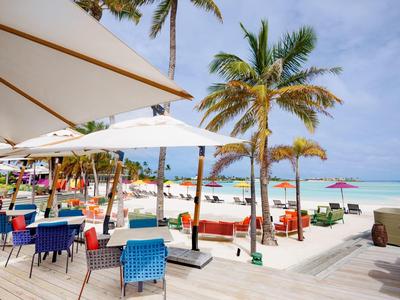 Strandrestaurant mit bunten Stühlen, Sonnenschirmen und Palmen am weißen Sandstrand.