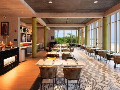 Modernes Restaurant mit großen Fenstern, Holzboden, gemustertem Teppich und gedeckten Tischen.