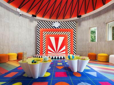 Bunter Kinderspielraum mit rundem roten Dach und Teppich, kleinen weißen Tischen und Sitzkissen.
