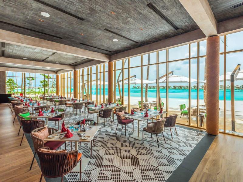 Elegantes Restaurant mit großen Glasfenstern, modernen Stühlen und Blick auf den Strand.