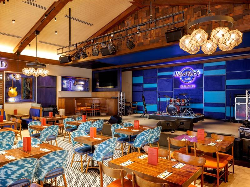 Gemütliches Restaurant mit Holzbalken, gemusterten Stühlen, bunten Wänden und Bühnenbeleuchtung.