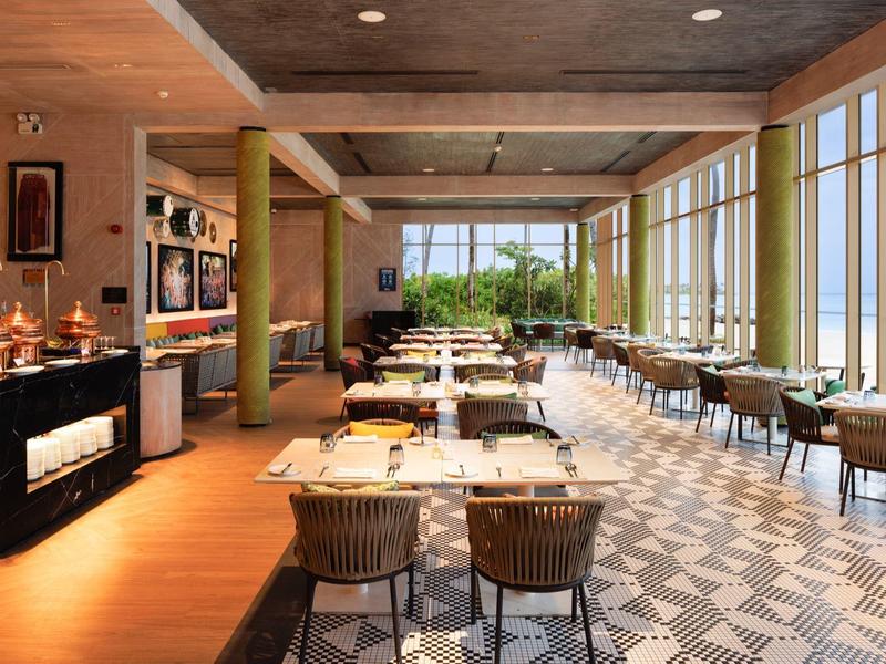 Modernes Restaurant mit großen Fenstern, Holzboden, gemustertem Teppich und gedeckten Tischen.