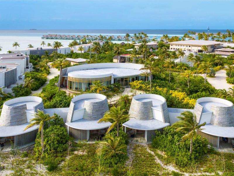 Moderne Rundhäuser mit flachen Dächern, umgeben von üppigem Grün nahe einem blauen Meer.