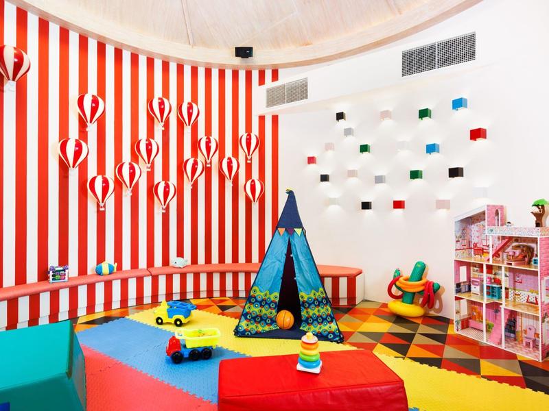 Buntes Kinderspielzimmer mit Zelt, buntem Teppich, Spielzeugautos und Regalen voller Spielzeug.