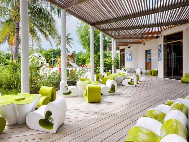 Terrasse mit weiß-grünen Sitzmöbeln, Holzdecke, Palmen und grüner Garten im Hintergrund.