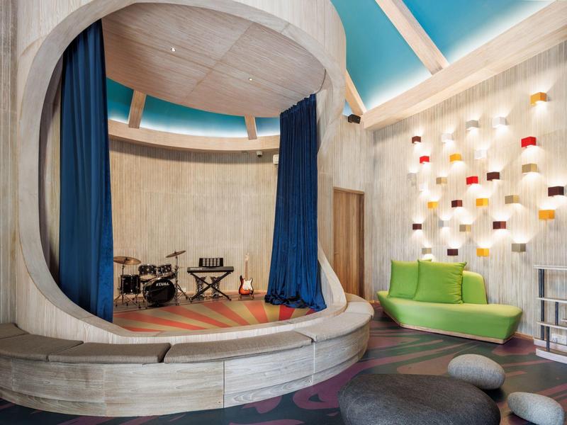 Moderner Raum mit rundem Podium, blauen Vorhängen, grüner Couch und Wand mit bunten Lampen.