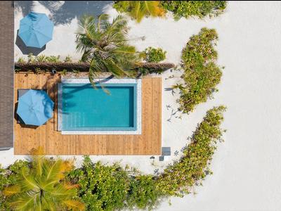 Aerial view of a pool with wooden deck, blue umbrellas, and surrounding greenery in a hotel vacation.