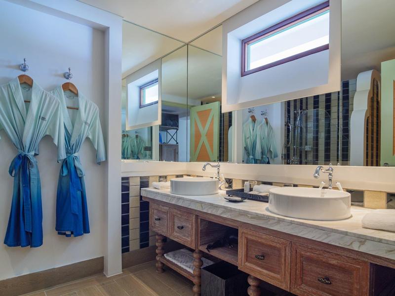 Nowoczesna łazienka z dwiema umywalkami, drewnianymi szafkami i dwoma niebieskimi szlafrokami na ścianie.