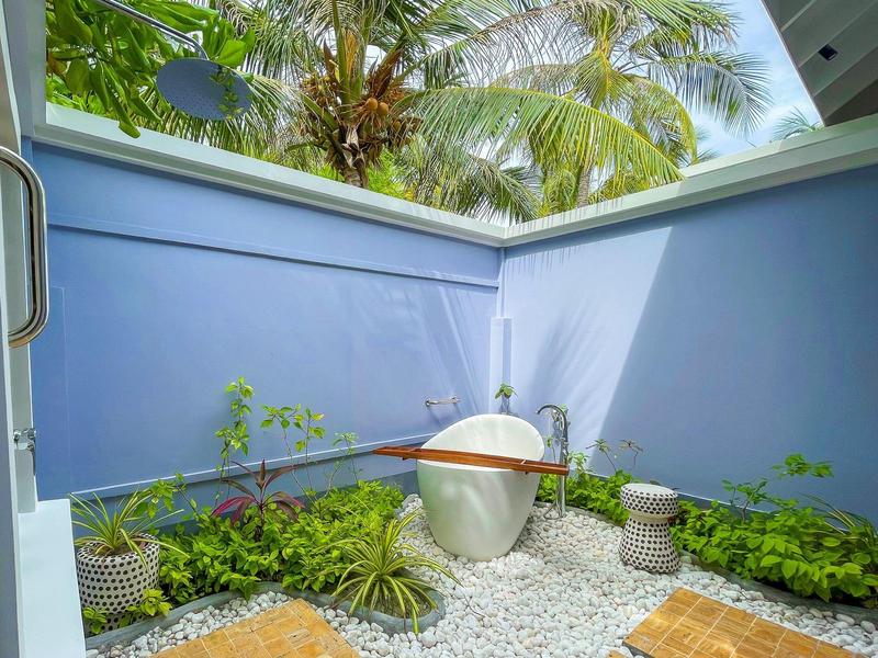 Mały teren na zewnątrz z niebieskimi ścianami, roślinami i białymi kamykami obok nowoczesnej umywalki.