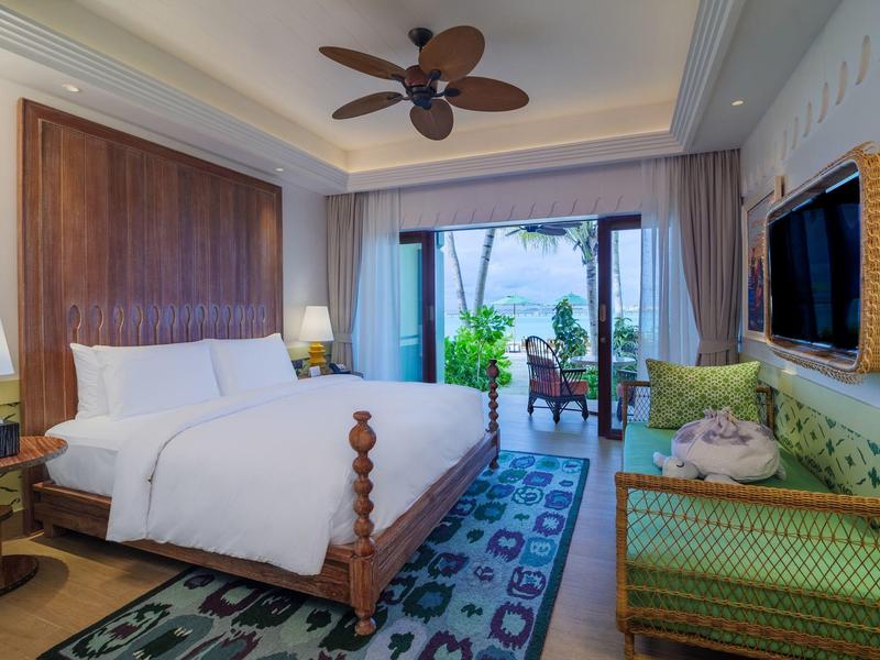 Przytulny pokój hotelowy z dużym łóżkiem, wentylatorem sufitowym i balkonem z widokiem na rośliny.