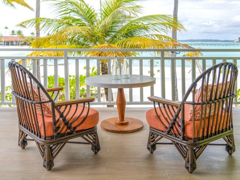 Dwa krzesła z rattanu z pomarańczowymi poduszkami i okrągły stół na werandzie z widokiem na morze