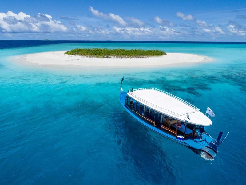 Klares türkisfarbenes Meer mit einem kleinen grünen Inselchen und einem weißen Boot mit Dach.