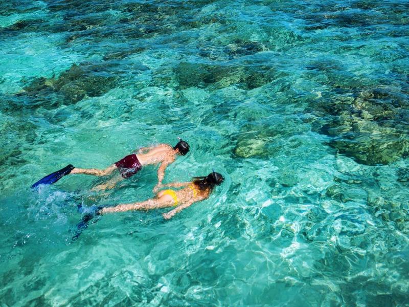Zwei Personen schnorcheln im klaren, türkisfarbenen Wasser mit sichtbarem Meeresboden.