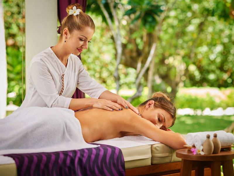 Frau bekommt Rückenmassage auf Liege im hellen, grünen Garten mit ruhiger Atmosphäre.