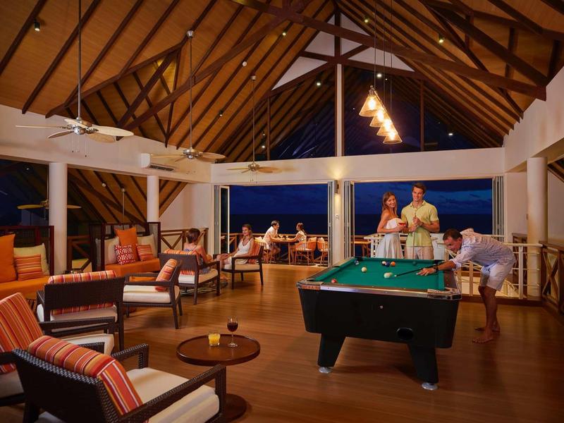 Großer, gemütlicher Wohnraum mit Holzbalken, Billardtisch und Sitzgruppen, offen zum Abendhimmel.