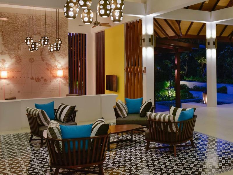 Modernes Wohnzimmer mit gemustertem Boden, Holzmöbeln und bunten Kissen unter Kronleuchtern.