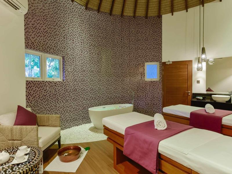 Gemütlicher Wellnessraum mit zwei Massageliegen, buntem Mosaik an der Wand und warmem Holzboden.