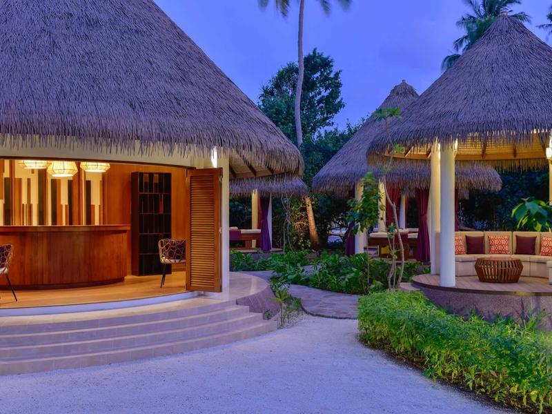 Tropisches Resort mit Strohdachhäusern, abendlicher Beleuchtung und gepflegten Gartenwegen.