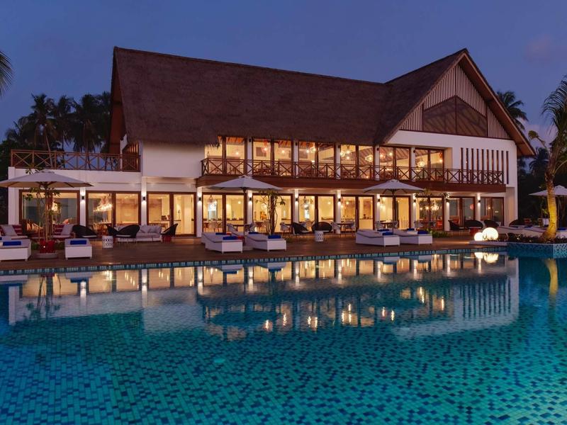 Großes Haus mit vielen Fenstern, beleuchtet und spiegelnd im ruhigen blauen Pool bei Abenddämmerung.