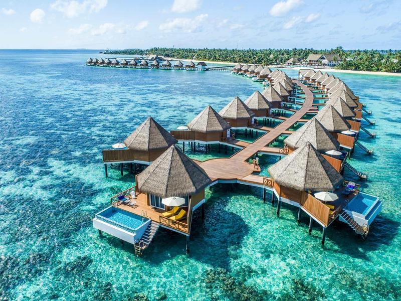Überwasserbungalows mit Strohdächern auf türkisfarbenem Meer, verbunden durch Holzstege.