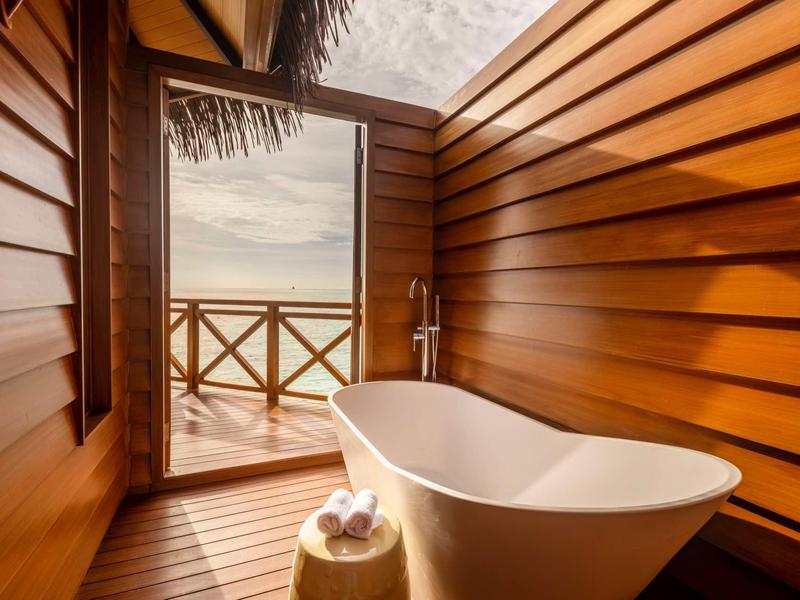 Holzbad mit freistehender Badewanne, Handtüchern und Meerblick durch offene Tür zum Balkon.