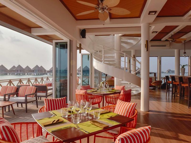 Helles Restaurant mit Holzdecke, rot gestreiften Sesseln und großer Fensterfront mit Aussicht aufs Wasser.