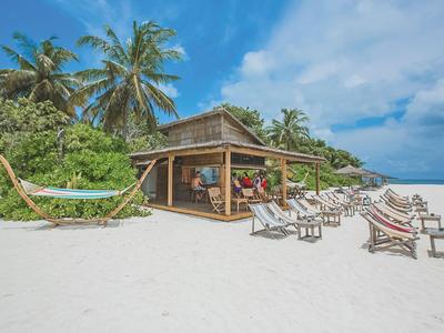 Bungalow sulla spiaggia con lettini e amaca su sabbia bianca sotto cielo azzurro