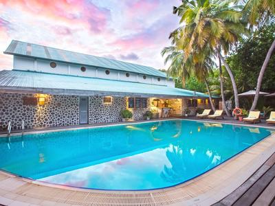 Grande piscina accanto a una casa in pietra con palme e lettini al tramonto.