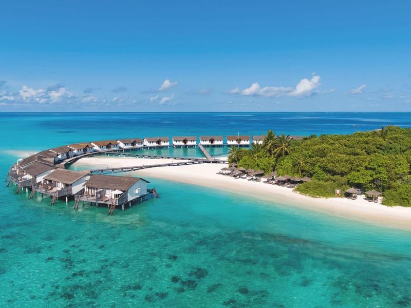 Lussuosi bungalow sull'acqua su una spiaggia tropicale con acqua turchese limpida.
