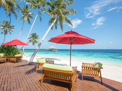 Strandterras met rode parasols, houten stoelen en palmbomen bij turquoise zee