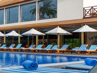 Zwembadgebied met blauwe ligstoelen, parasols en moderne gebouwgevels op de achtergrond.