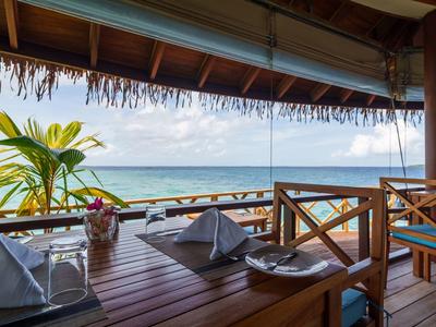 Gedekte tafel op een terras met uitzicht op zee en palmbomen onder een houten dak.