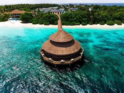 Rundes Restaurant auf Stelzen über klarem, türkisfarbenem Wasser mit einem Sandweg zur Insel.