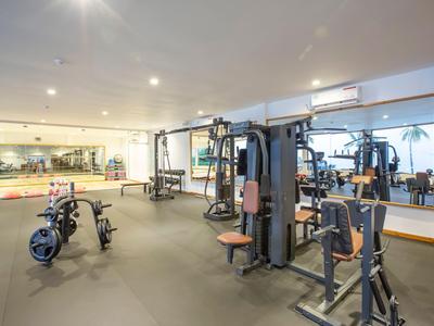 Heller Fitnessraum mit verschiedenen Trainingsgeräten und großen Spiegeln an der Wand.