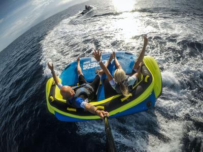 Drei Personen sitzen auf einem aufblasbaren Wasserspielzeug, gezogen von einem Boot auf dem Meer.