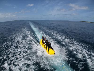 Drei Personen sitzen auf einem gelben Bananenboot, das über das Meer gezogen wird.