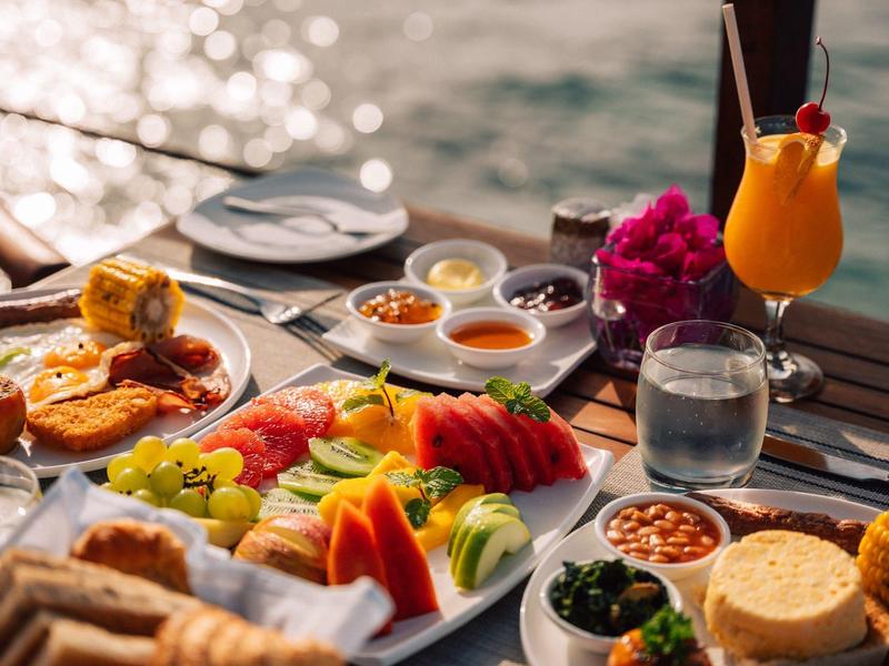 Ontbijttafel met vers fruit, gebak en drankjes met uitzicht op zee.