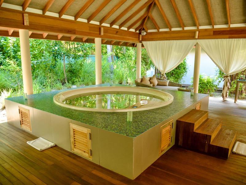 Ronde buitenjacuzzi onder houten dak met uitzicht op groene planten