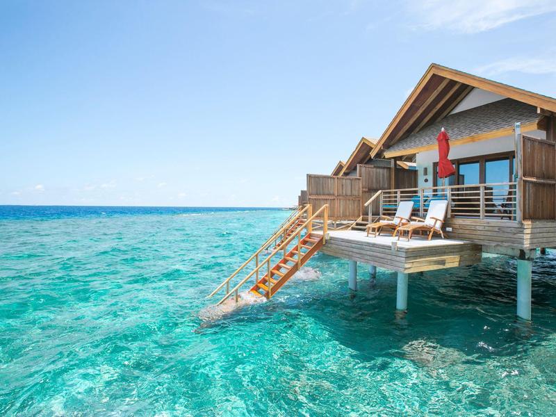 Bungalow boven helder turquoise water met trap naar zee en een parasol.