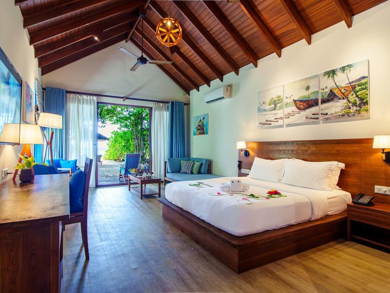 Gezellige hotelkamer met houten balkenplafond, groot bed en uitzicht op een terras met groen.