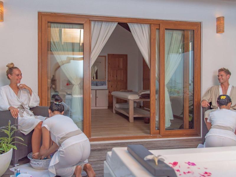 Twee vrouwen genieten van een pedicure op het terras van een hotelkamer met uitzicht op een ligstoel.