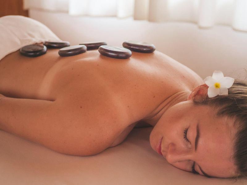 Vrouw ligt ontspannen op haar zij met warme stenen op haar rug in een lichte kamer.