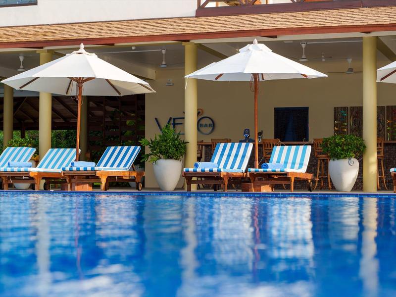 Blauw zwembad met ligstoelen en witte parasols voor een hotelgebouw