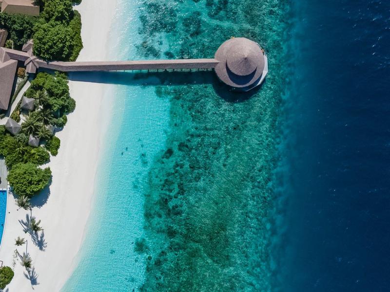 Luchtfoto van een strandresort met wit zand, een lange pier en helder blauw water.