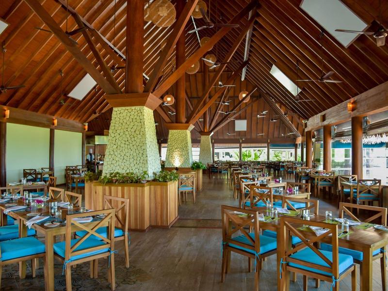 Grote restaurantruimte met houten plafond, blauwe kussens en een centraal open haard.