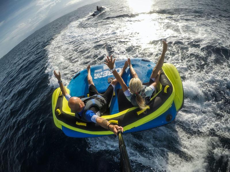 Drie mensen zitten op een opblaasbaar waterspeelgoed dat door een boot wordt getrokken.