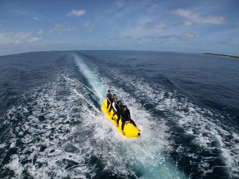 Drie personen varen op een gele banaanboot over de open zee bij een gedeeltelijk bewolkte hemel.