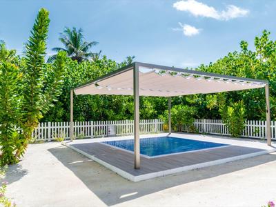 Ein kleiner Pool im Freien mit einem modernen Sonnenschutzdach und umgeben von grünem Laub.